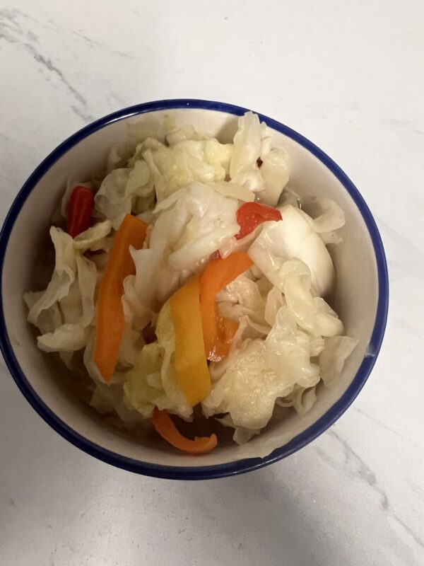 A bowl of food with cabbage and peppers.